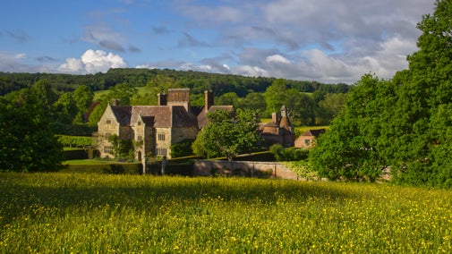 Sandstone house and garden in a valley with wooded countryside and field with buttercups